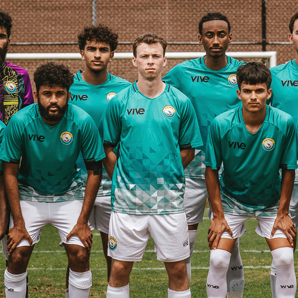 Group of soccer players wearing teal jerseys with 'vive' branding on a sports field.