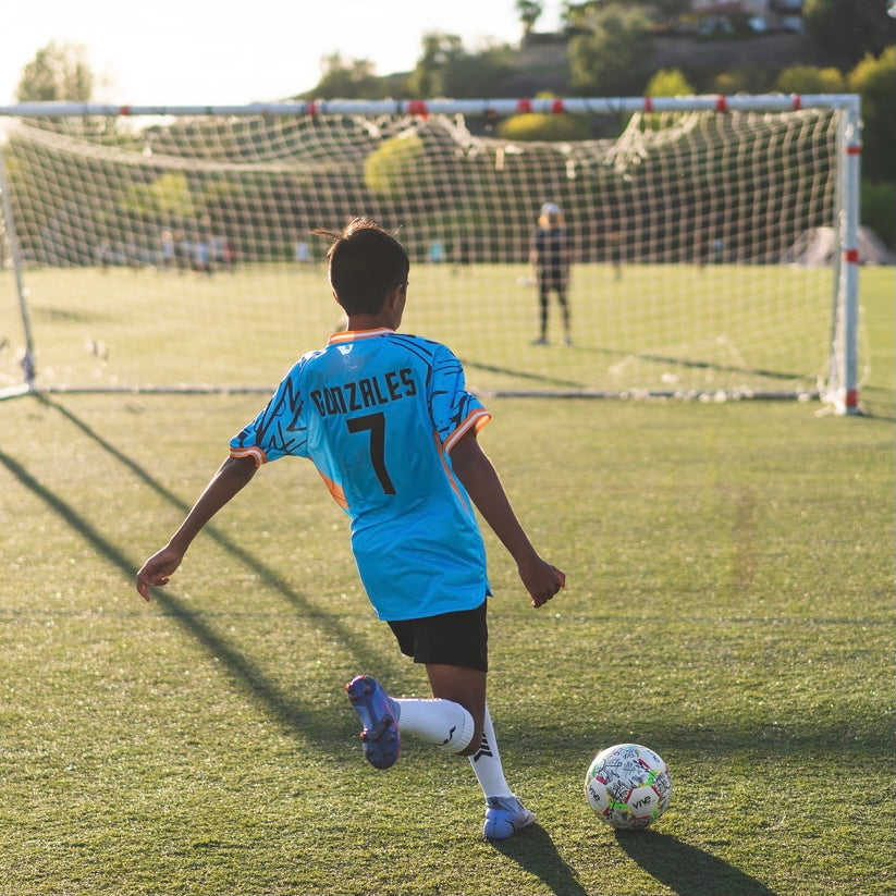 Campeones Size 5 Soccer Ball on soccer field kid kicking goal - White color with Black artwork design with red yellow green trim from Vive